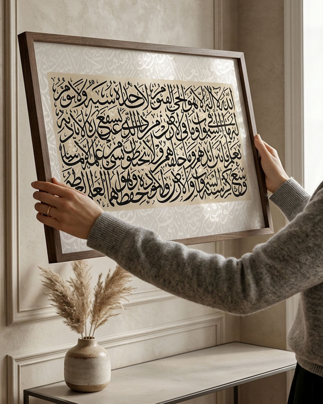 Ayatul Kursi canvas in a gold frame being hung on a pale wall